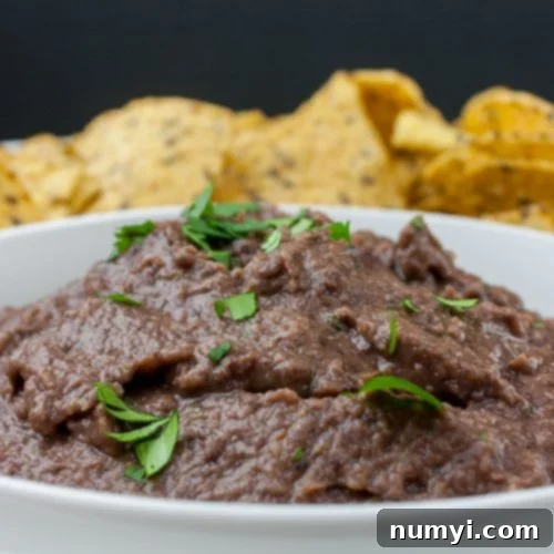 Easy Black Bean Dip in a white bowl with tortilla chips in the distance.