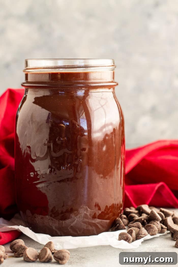 A jar of homemade hot fudge sauce. The rich, dark chocolate sauce gleams, inviting a taste. It's a perfect topping for any dessert.