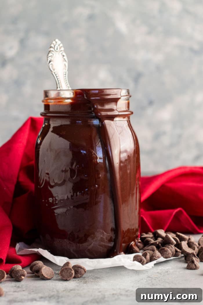 A jar of hot fudge sauce with a spoon in it and a drip of sauce going down the side of the jar, ready to be enjoyed.