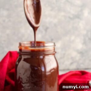 A spoon pulled straight up from a jar of homemade hot fudge sauce letting it drizzle back into the jar.
