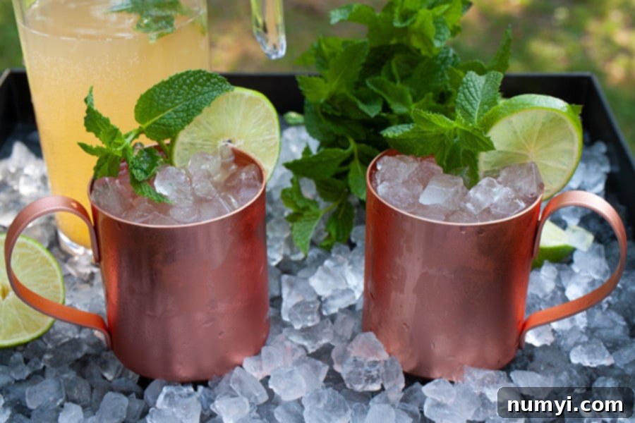 Two glistening Skinny Moscow Mules in elegant copper mugs, beautifully garnished with fresh mint sprigs and vibrant lime slices, resting on a bed of crushed ice on a stylish serving tray. This image perfectly captures the refreshing and inviting essence of a low-carb, sugar-free cocktail.