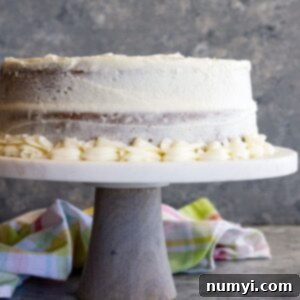 A cake on a stand covered in cream cheese frosting.