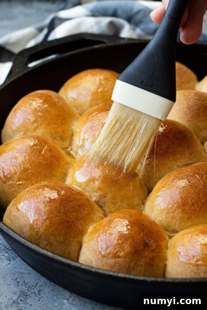 Melted butter being brushed on freshly baked honey wheat dinner rolls, a perfect side for any meal.