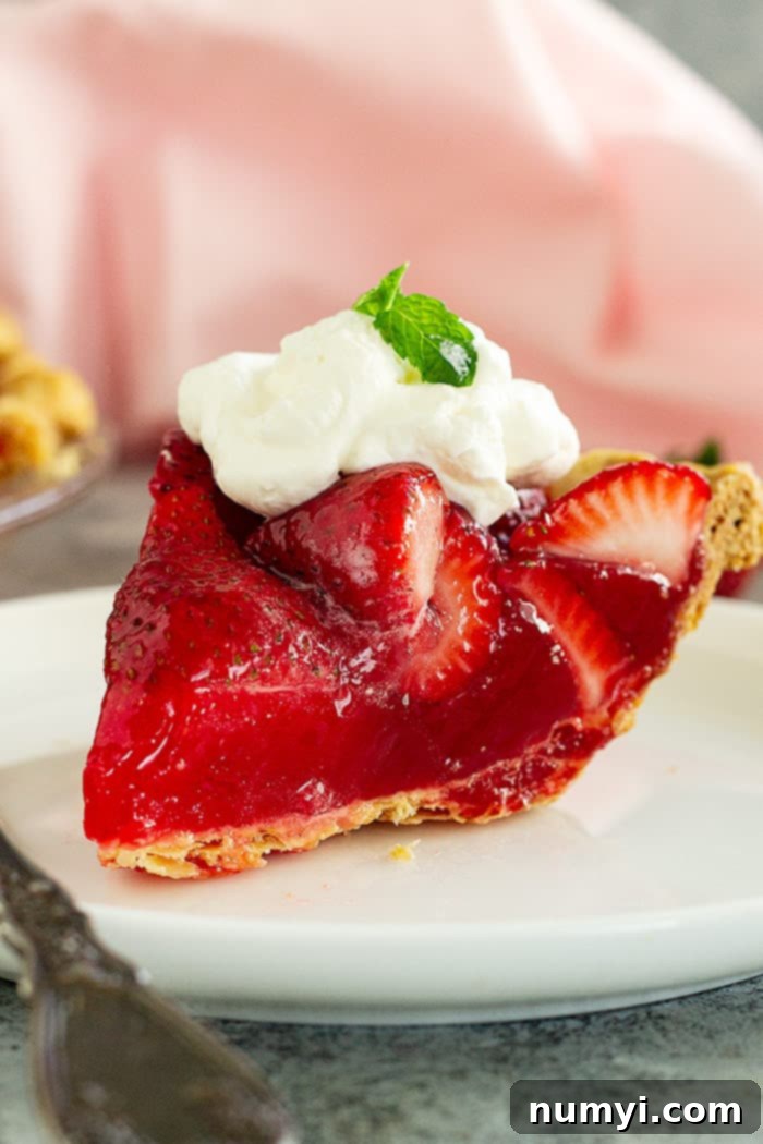 A piece of strawberry pie on a white plate topped with whipped cream and mint. 