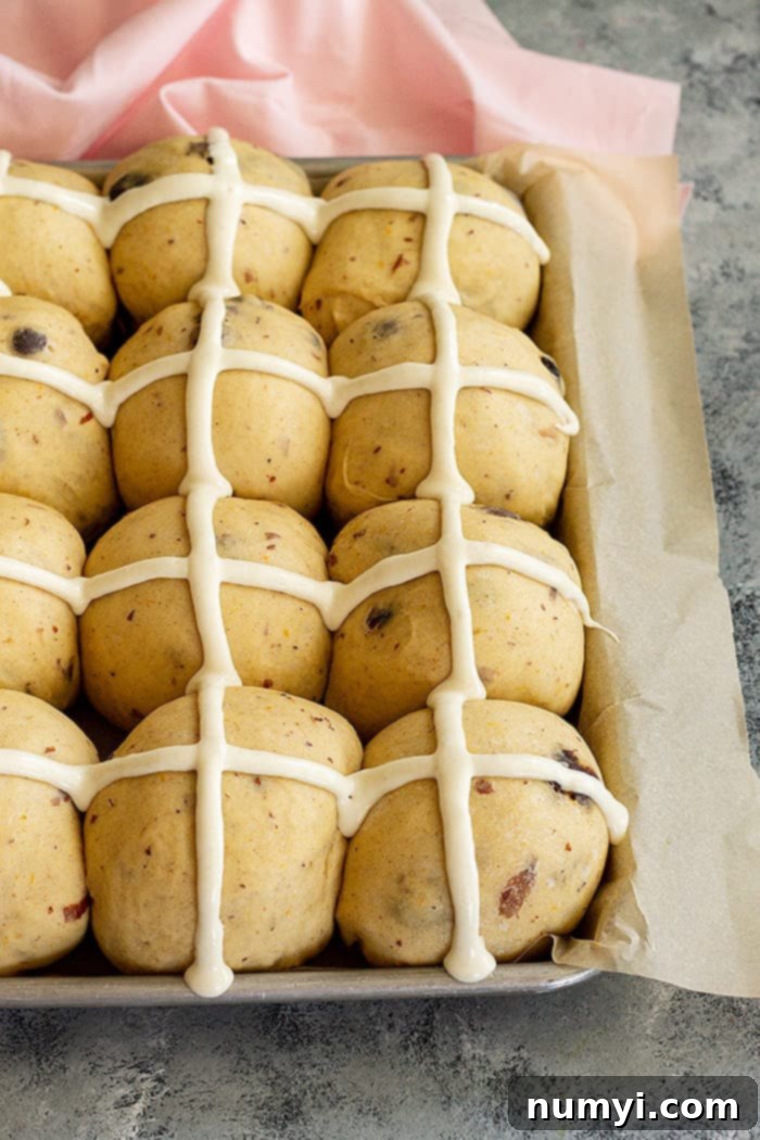 Close-up shot showing the traditional flour paste cross being piped onto unbaked hot cross buns.