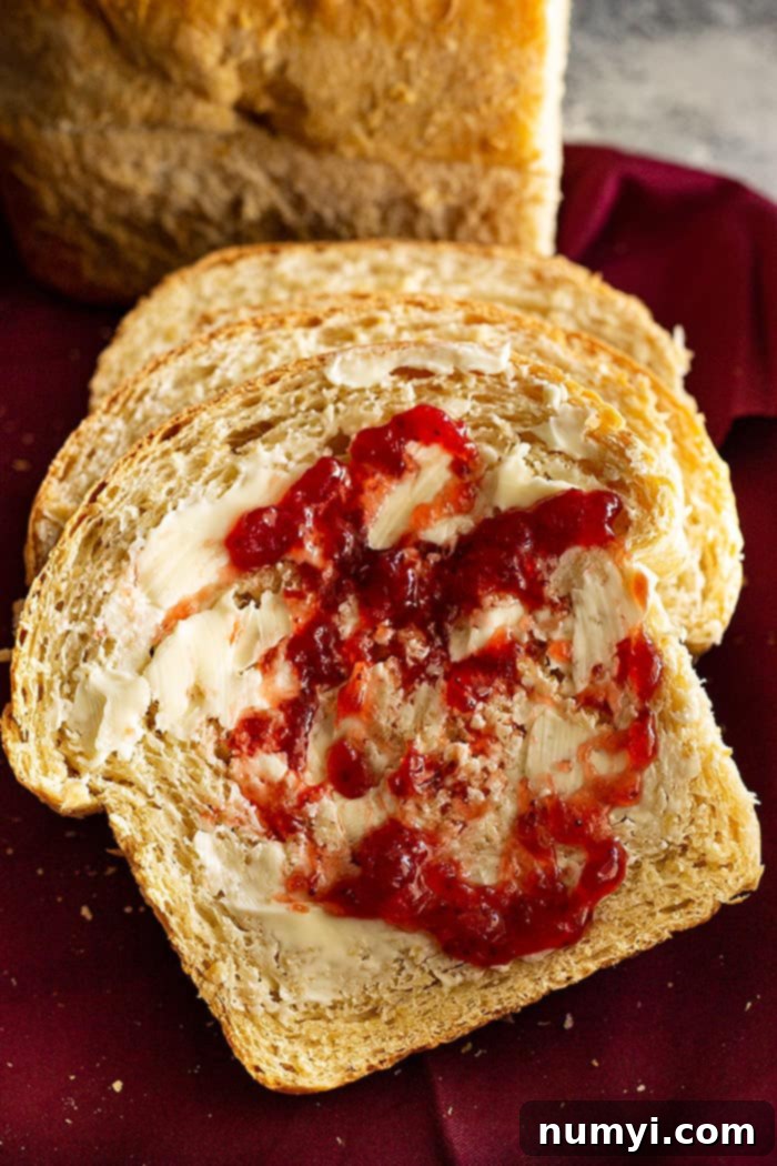 A slice of oatmeal sandwich bread smeared with butter and jam.