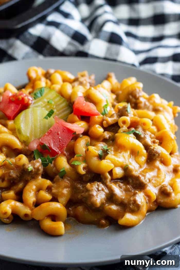A close up of cheeseburger pasta on a plate topped with chopped tomato and pickles.