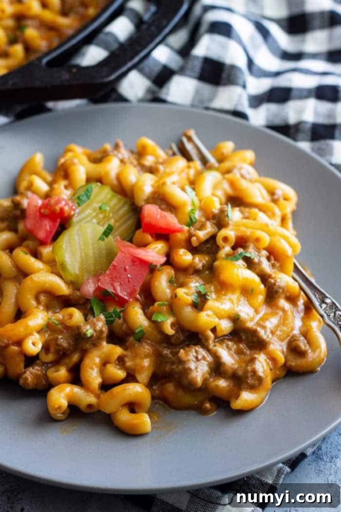 A plate of cheeseburger pasta topped with chopped parsley and tomato.