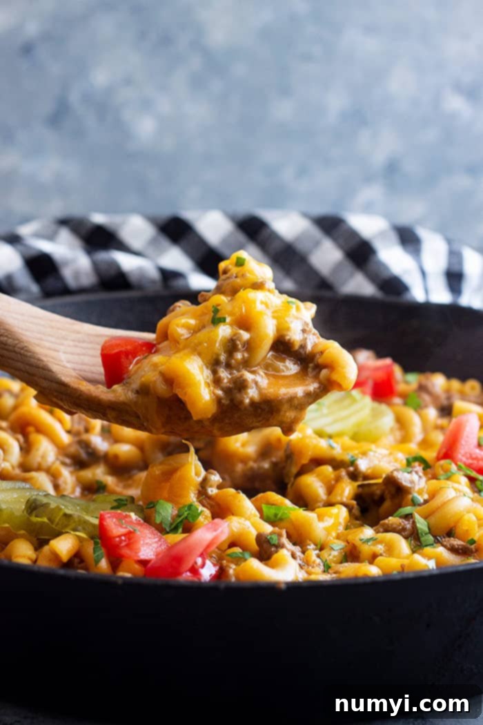 A skillet of cheeseburger pasta with a spoon pulling up a serving.