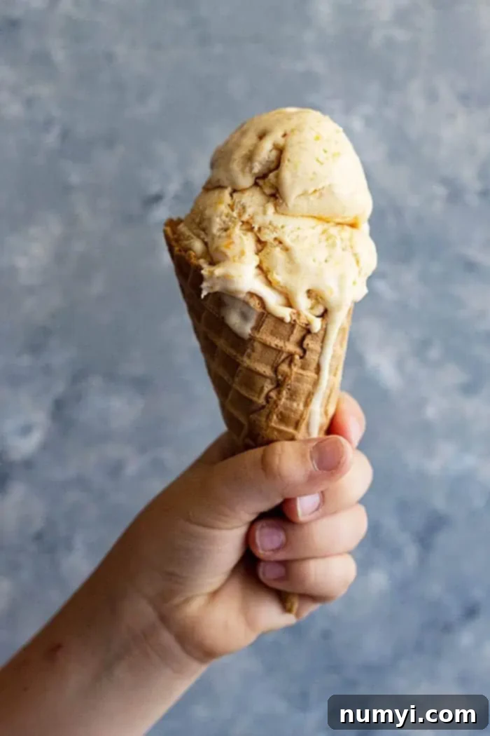 A child's hand holding up an ice cream cone with creamy peach ice cream, highlighting the perfect summer treat.