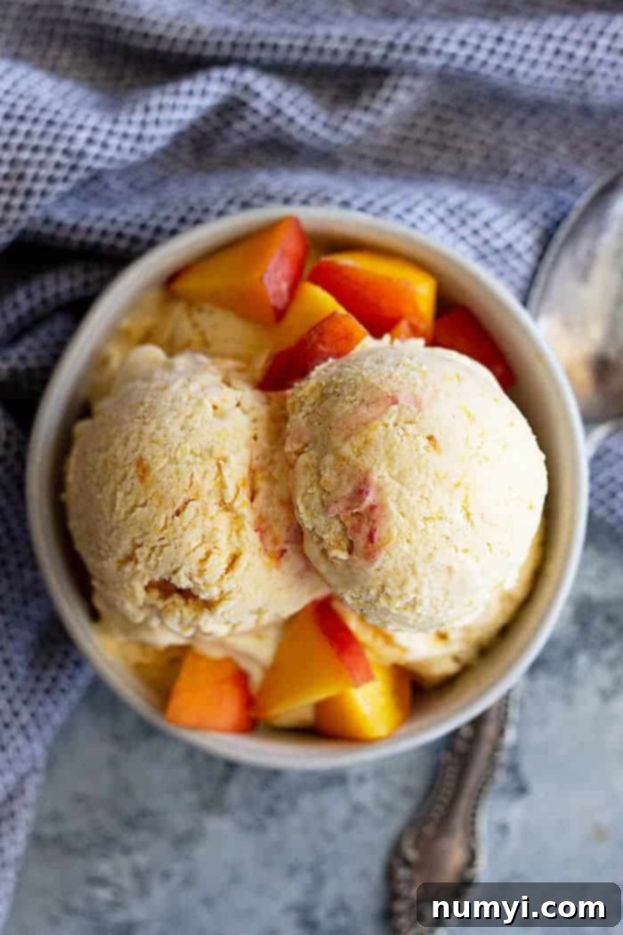 Overhead view of a bowl of creamy no-churn peach ice cream, garnished with fresh peach slices and a mint sprig.