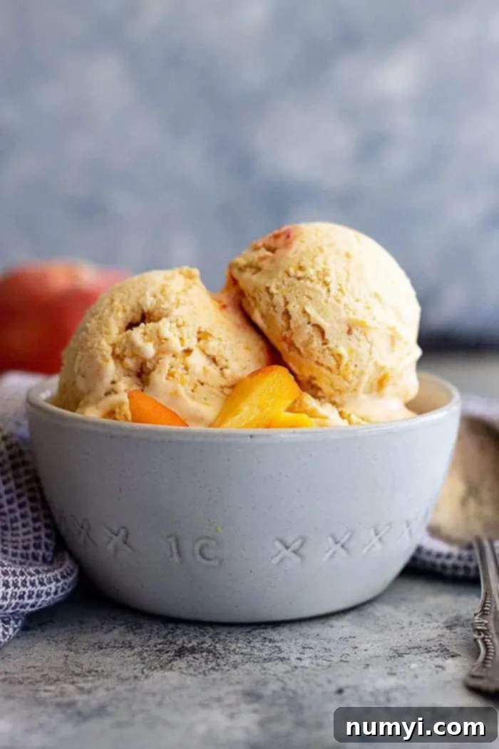 Close-up side view of a bowl of creamy homemade peach ice cream, topped with fresh peach slices, ready to be enjoyed.