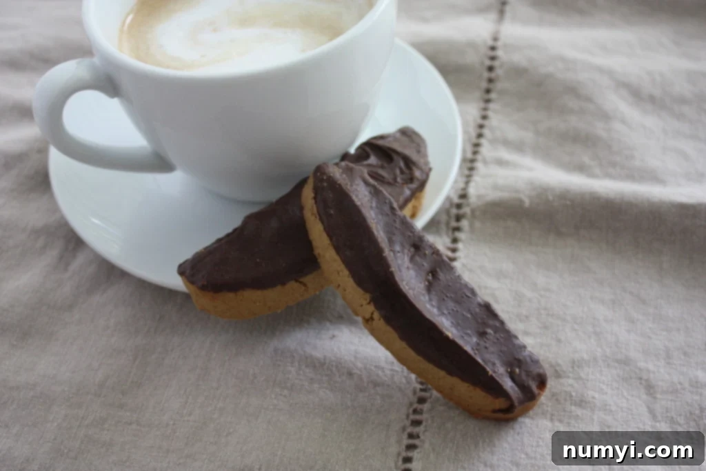 Espresso biscotti resting next to a latte, showcasing their perfectly dipped chocolate ends.