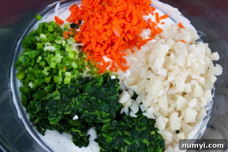 Cream base with spinach, onions, grated carrots and water chestnuts on top, ready to be mixed for the homemade spinach dip.