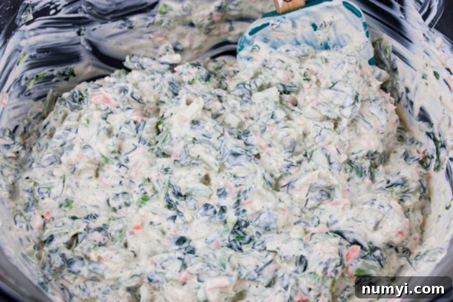 All ingredients for easy spinach dip mixed together in a glass mixing bowl, showing the vibrant colors.