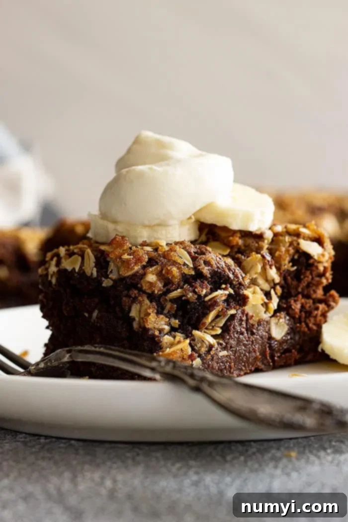 Decadent Banana Fudge Cake 2 A slice of rich fudge banana cake topped with light whipped cream and fresh banana slices, showcasing the melted chocolate pockets and oat crumble.