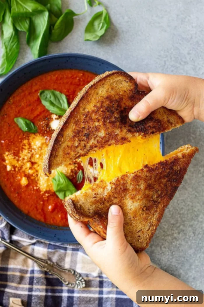 Hands pulling apart a grilled cheese sandwich over a bowl of soup.