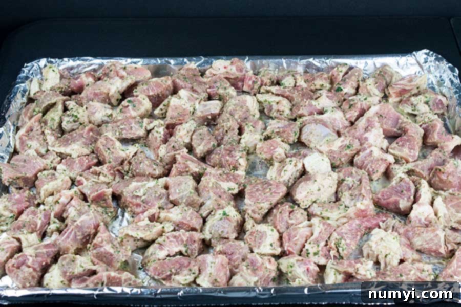 Marinated pork cubes neatly arranged in a single layer on a foil-lined baking sheet, ready for the oven.