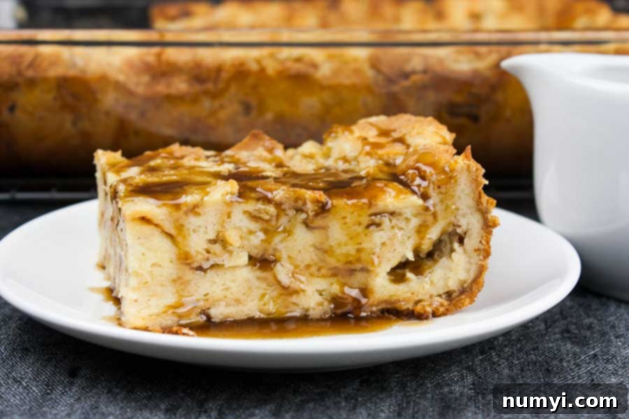 A slice of bread pudding on a white plate drizzled with bourbon sauce, ready to be enjoyed.