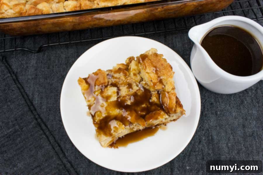 Close-up of a slice of bread pudding drizzled generously with bourbon sauce on a pristine white plate, showcasing its golden-brown crust and moist interior.