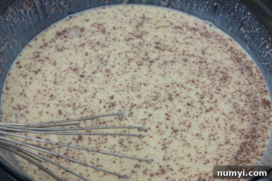 Close-up of the egg and milk mixture being whisked in a glass mixing bowl, showing the creamy texture and incorporation of ingredients.
