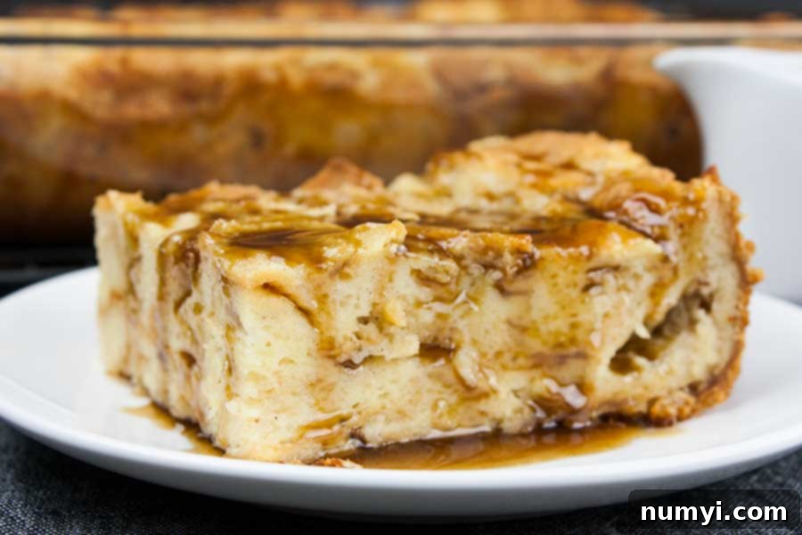 A single slice of bread pudding generously coated with bourbon sauce on a white plate, ready to be eaten.