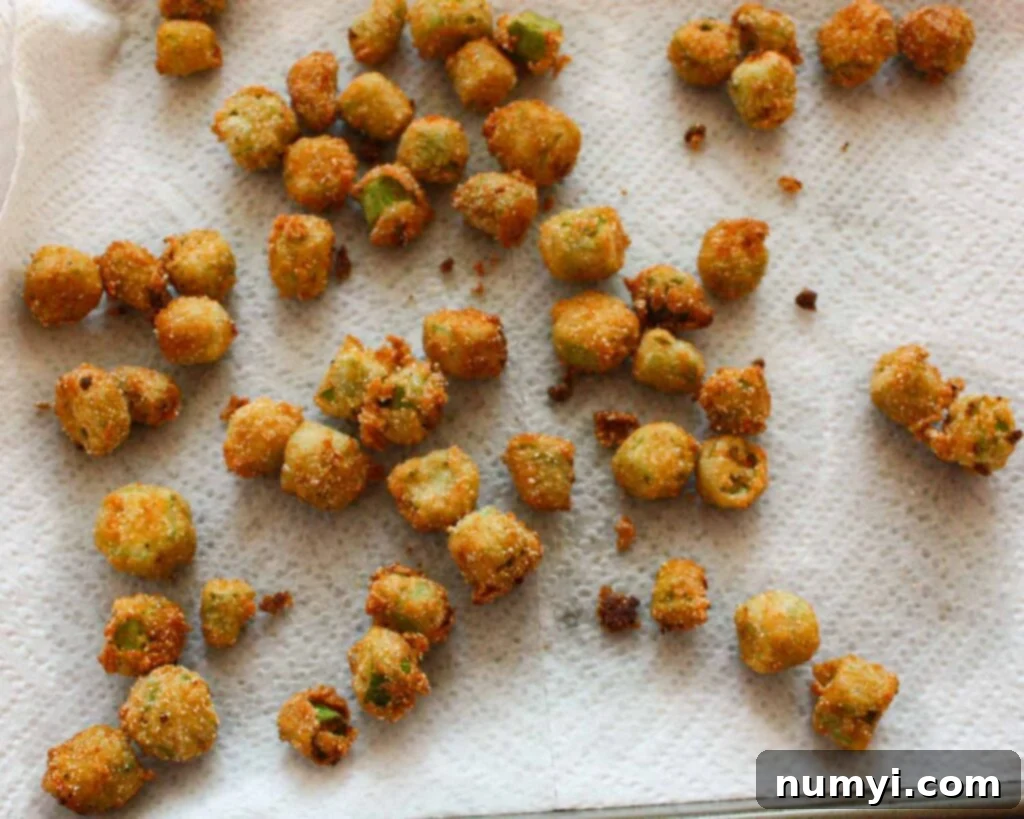 Buttermilk-Kissed Golden Okra: A Southern Crunch 4 Freshly fried okra, golden brown and glistening, draining on a sheet pan lined with paper towels.