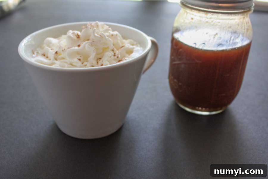 Pumpkin spice latte in a white cup topped with whipped cream and a bottle of homemade pumpkin spice syrup sitting next to it, evoking cozy autumn vibes.