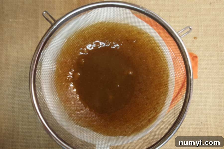 Freshly made pumpkin spice syrup being strained through a fine-mesh sieve into a clean bowl, ensuring a smooth texture.