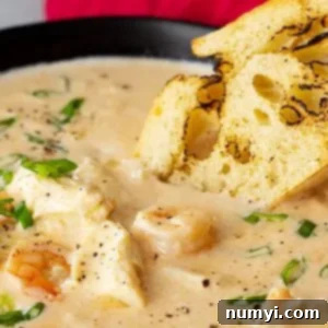 Close up of seafood bisque in a bowl with a piece of crusty bread dipping into it.