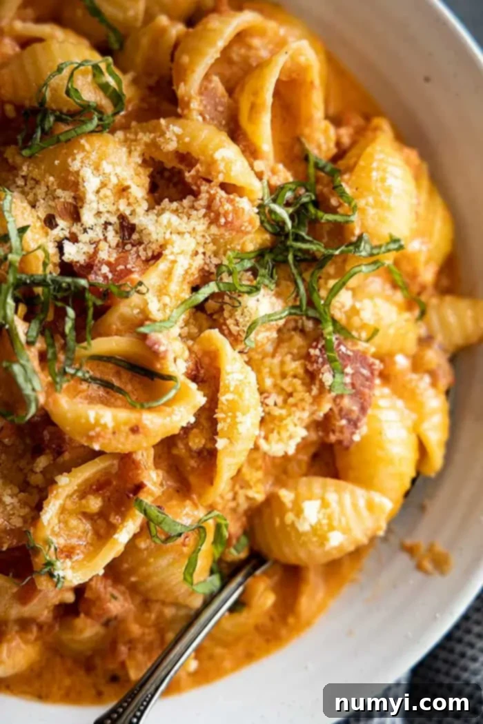 Easy Homemade Vodka Sauce 5 extreme closeup of the best vodka sauce generously coating pasta, adorned with fresh basil leaves and grated parmesan cheese