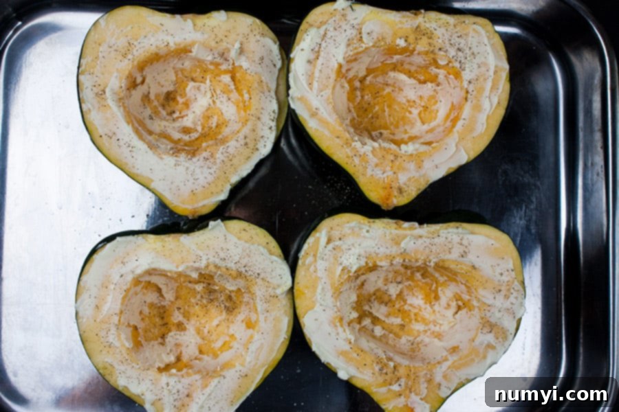 Raw acorn squash halves smeared with butter, salt, and pepper in a roasting pan, ready for the oven.