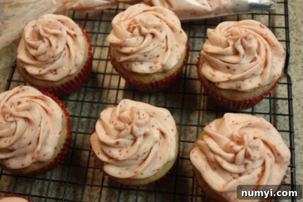 Fresh strawberry cupcakes topped with fresh strawberry buttercream icing on a wire rack.