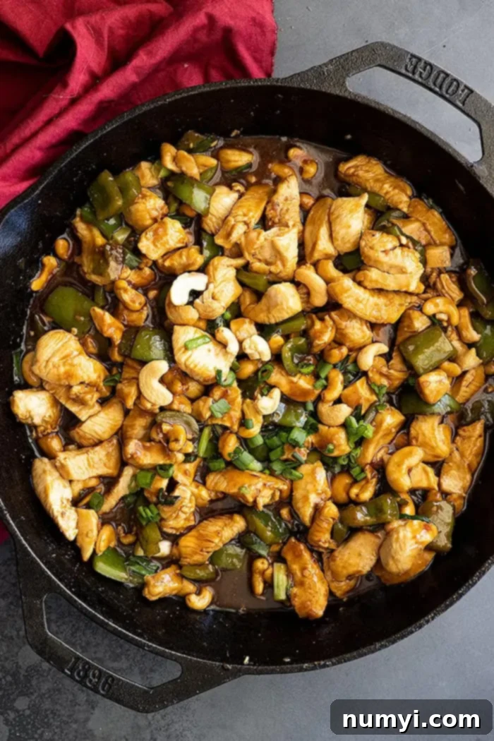 Overhead view of cashew chicken in a cast iron skillet garnished with green onions. Red napkin off to the side.