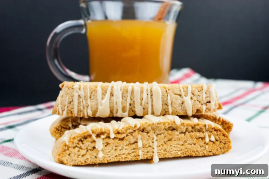 Spiced apple cider biscotti stacked on a white plate with a glass mug filled with apple cider behind them, highlighting the perfect fall treat.