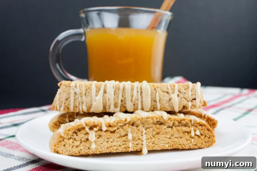 Spiced Apple Cider Biscotti arranged on a white plate with a glass mug of hot apple cider in the background, inviting a warm treat.