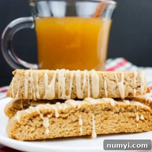 Spiced apple cider biscotti stacked on a white plate with a glass mug filled with apple cider behind them.