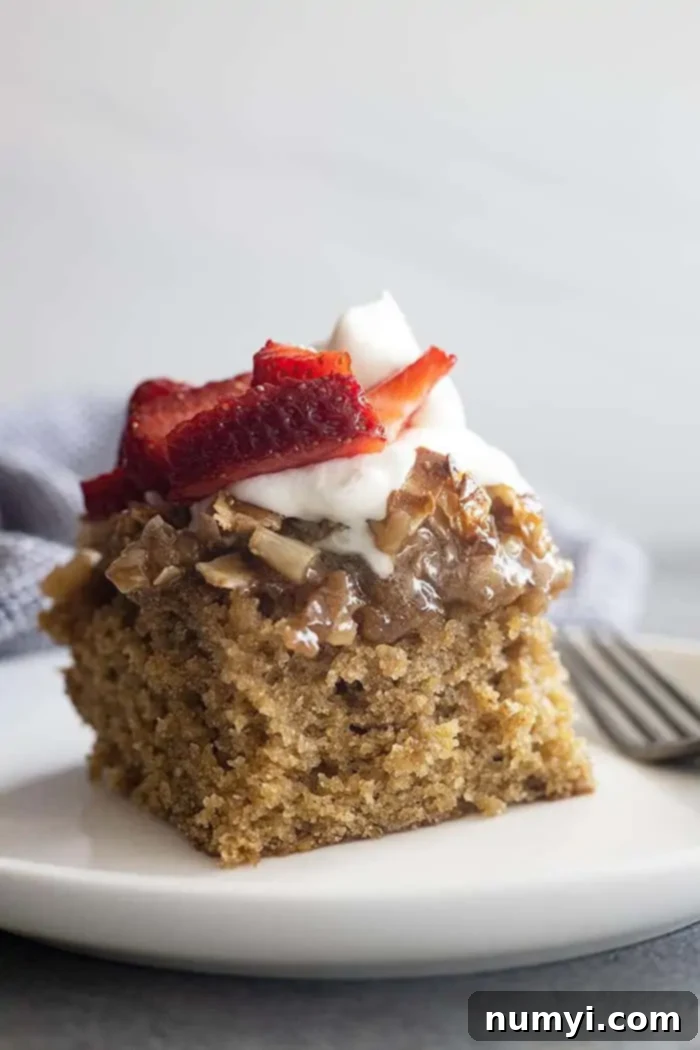Hearty Spiced Oatmeal Cake 2 A large slice of moist Old Fashioned Oatmeal Cake on a white plate, elegantly topped with whipped cream and fresh strawberries, showcasing its rich texture and delicious caramelized coconut and nut topping.