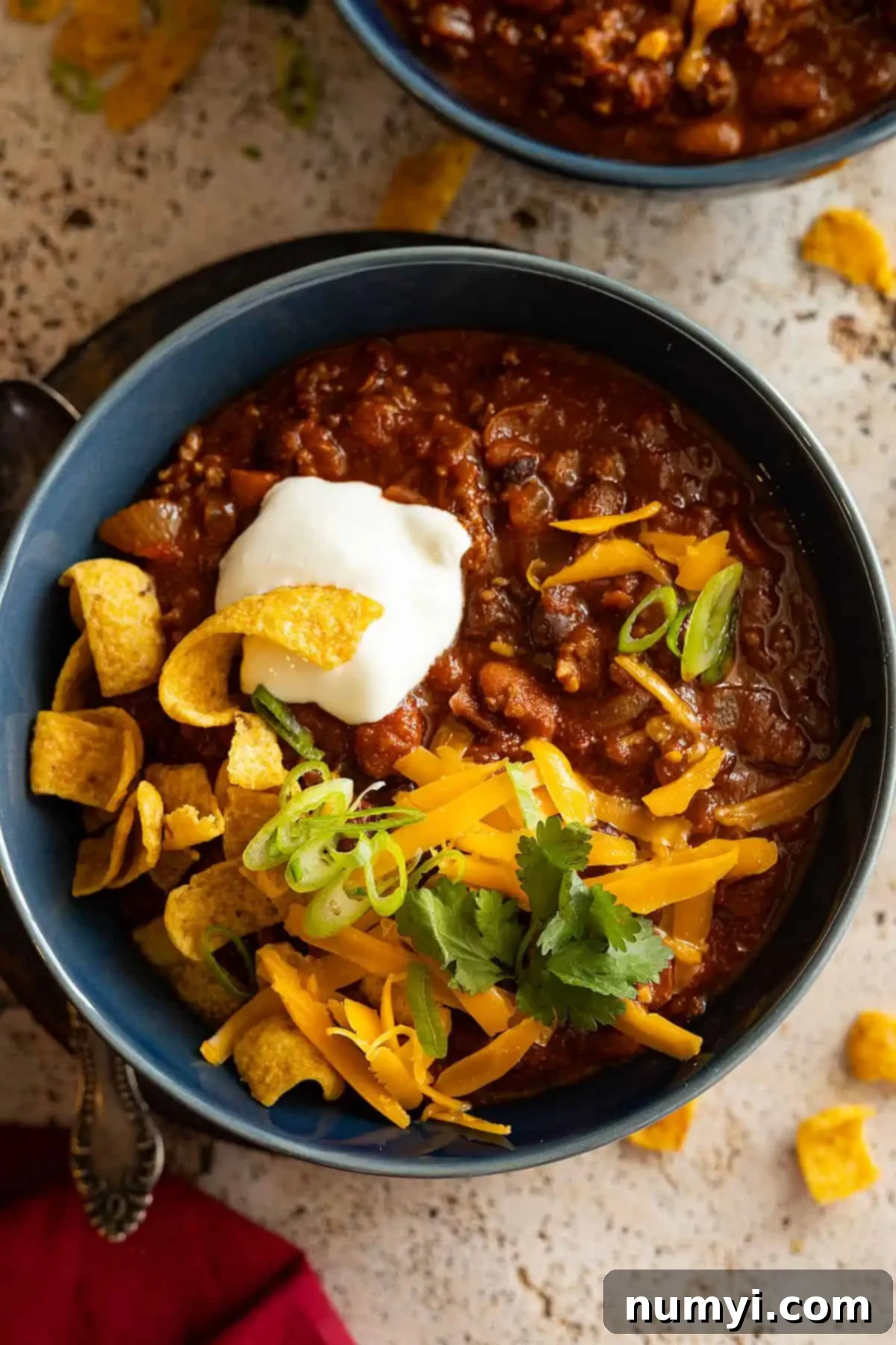 Overhead view of chili in a blue bowl topped with sour cream, cheese, and corn chips. 