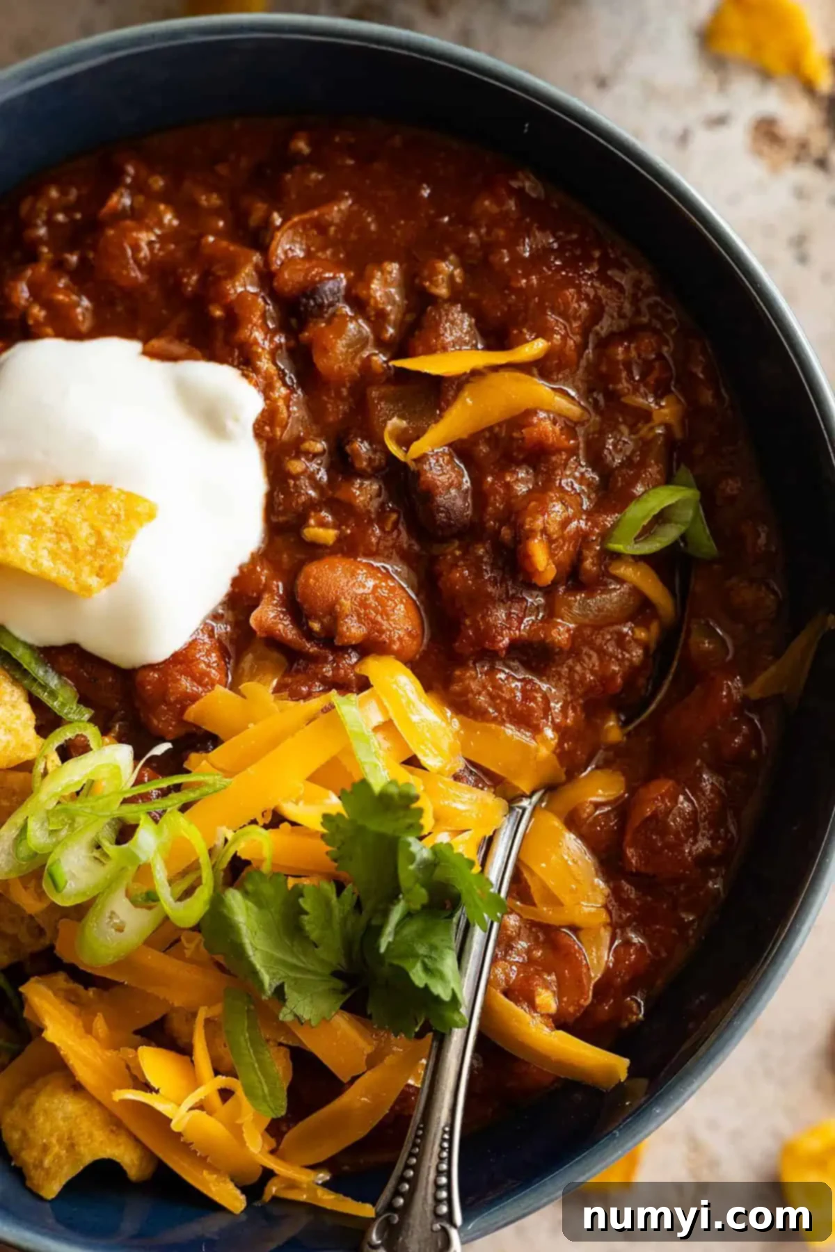 Overhead close up of chili in a bowl with sour cream, cheese, and green onion on top. 