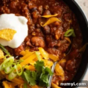 Overhead close up of chili in a bowl with sour cream, cheese, and green onion on top.