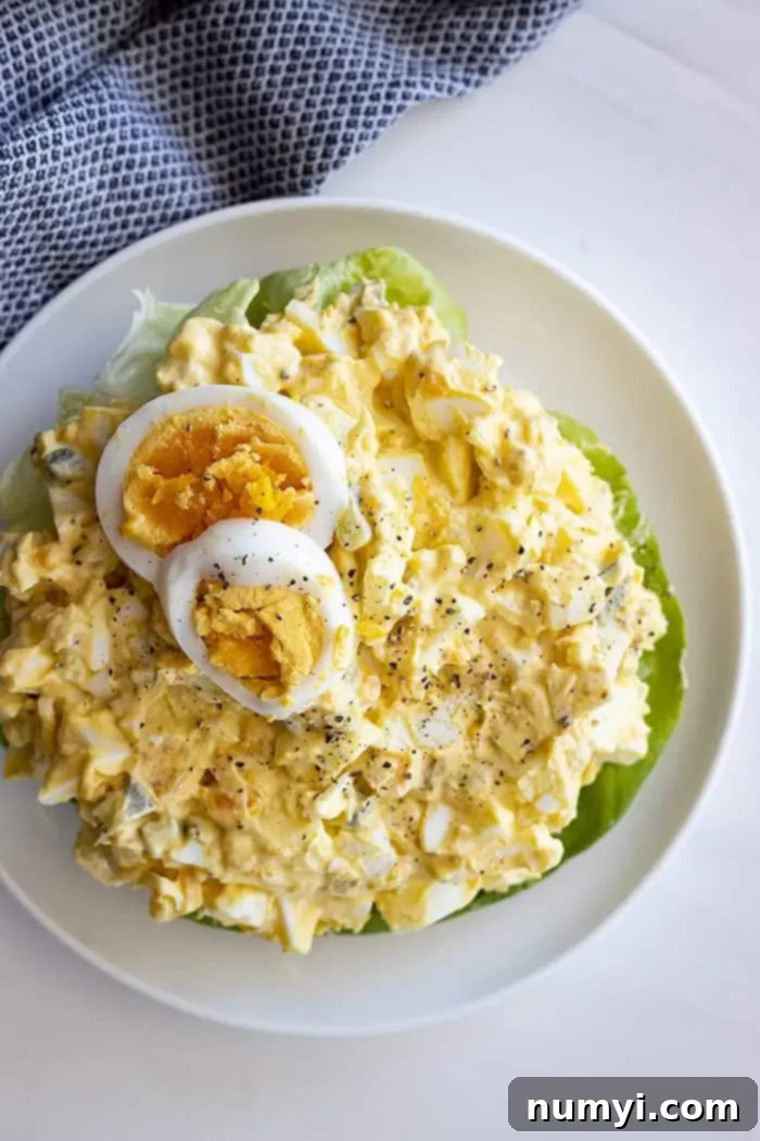 Irresistible Egg Salad 2 Overhead view of a large bowl of homemade egg salad, garnished with two slices of hard-boiled egg and fresh ground black pepper, ready to be served.