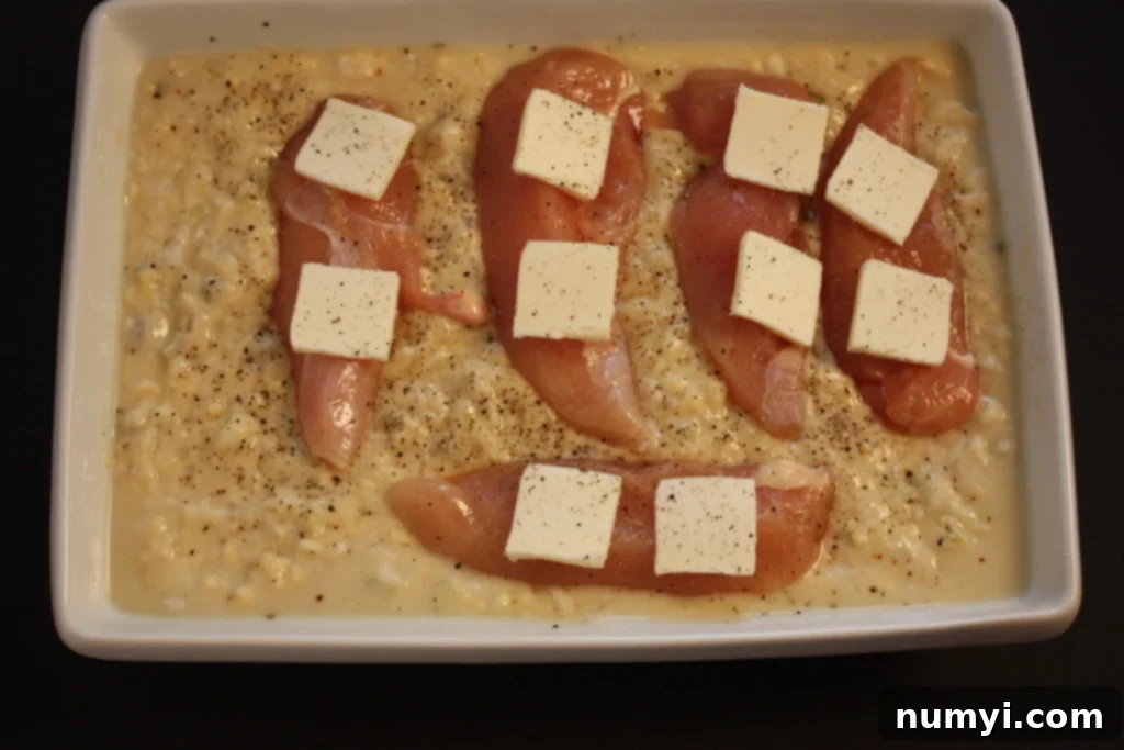Ingredients for creamy baked chicken and rice combined in a white casserole dish before baking.