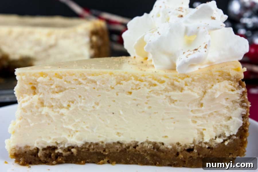 A slice of eggnog cheesecake with gingersnap crust on a white plate garnished with whipped cream and freshly grated nutmeg.