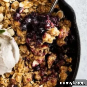 Close up of blueberry crisp with a spoon in it. Topped with a scoop of ice cream.