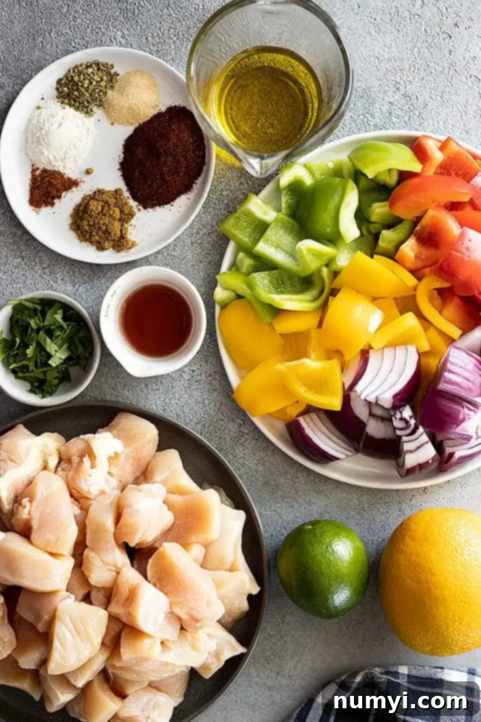 A vibrant selection of fresh ingredients laid out for making the best chicken fajita skewers, including colorful bell peppers, red onion, chicken breast, limes, orange, and various spices.
