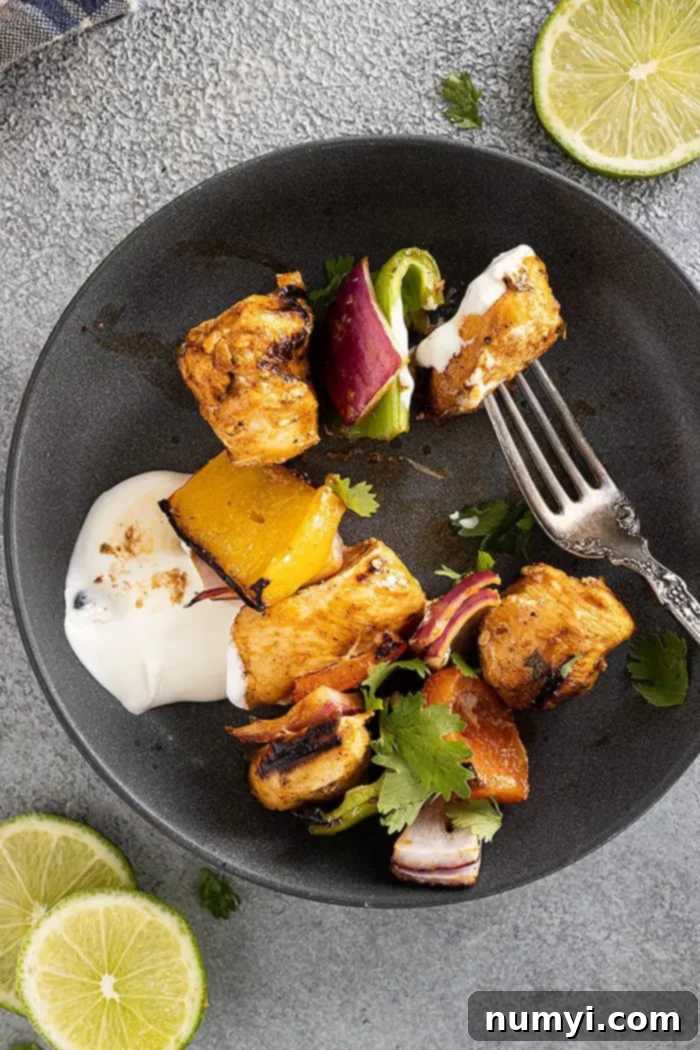 Cooked chicken and bell peppers removed from the skewer and served on a white plate with a dollop of sour cream and fresh cilantro garnish, ready to be enjoyed.