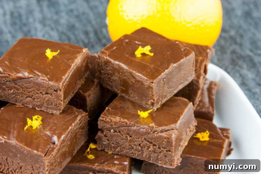 Chocolate orange fudge pieces garnished with orange zest stacked on a white plate and .