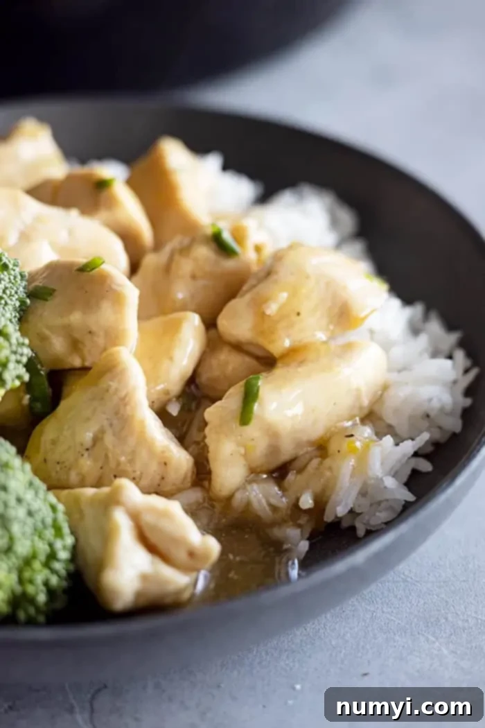 Close up of lemon chicken in a black bowl served over fluffy white rice.