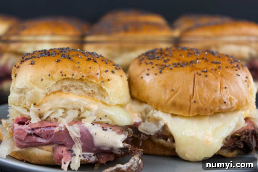 Close-up of golden brown Pastrami and Swiss cheese sliders, fresh out of the oven and garnished with poppy seeds.